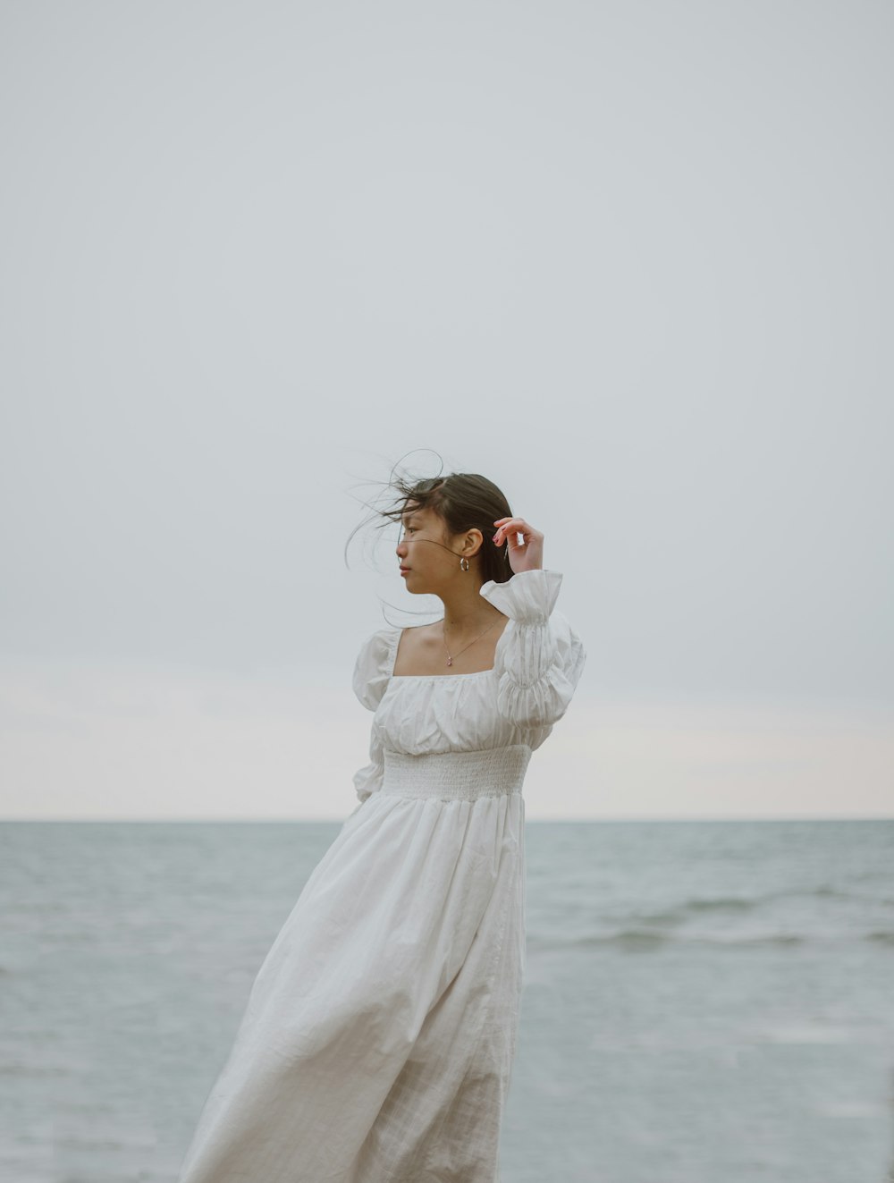 woman in white dress wearing black sunglasses standing near sea during daytime