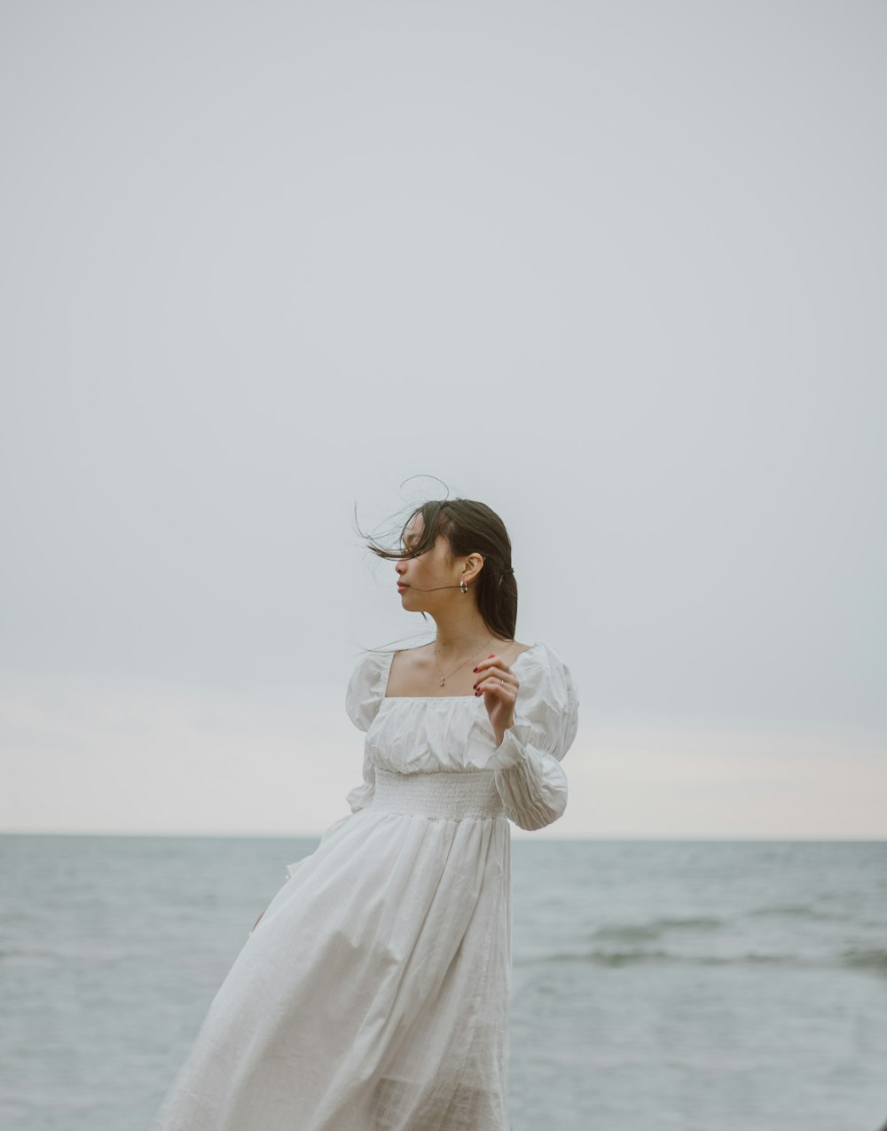 donna in abito bianco a maniche lunghe in piedi in riva al mare durante il giorno