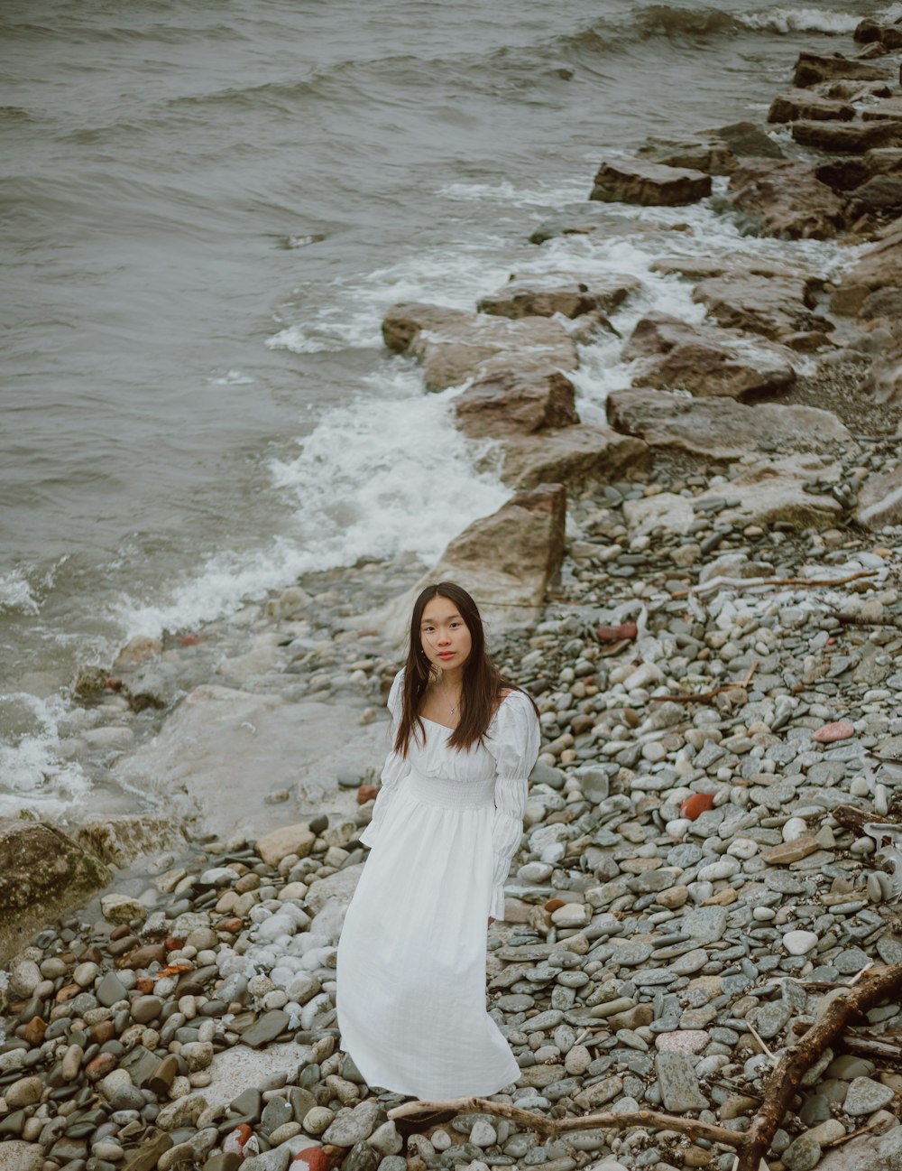 woman in white dress standing on rocky shore during daytime