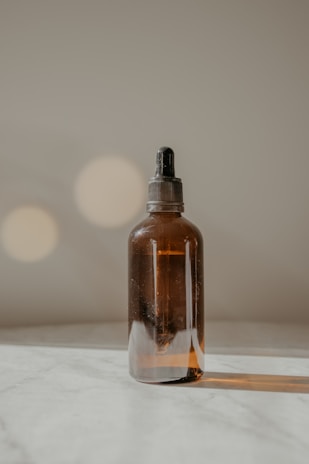 Close-up of a dark brown glass bottle of facial oil resting on a tan linen cloth with soft natural light.