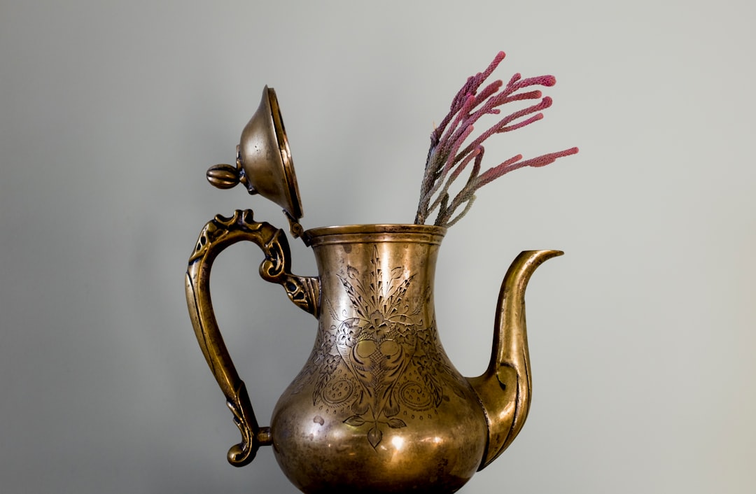 brass colored pitcher with white and red flower