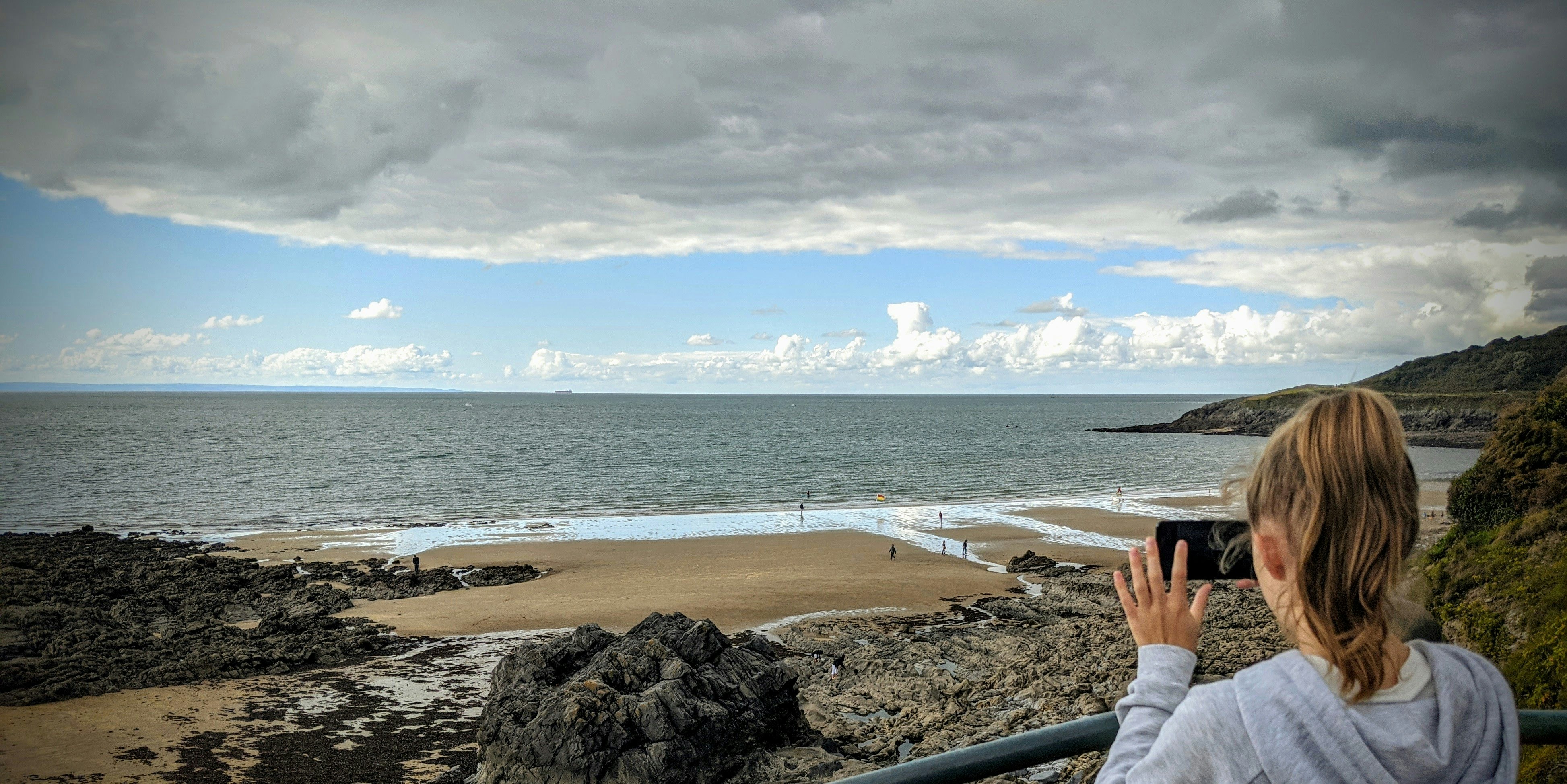 person in gray pants sitting on brown rock near body of water during daytime
