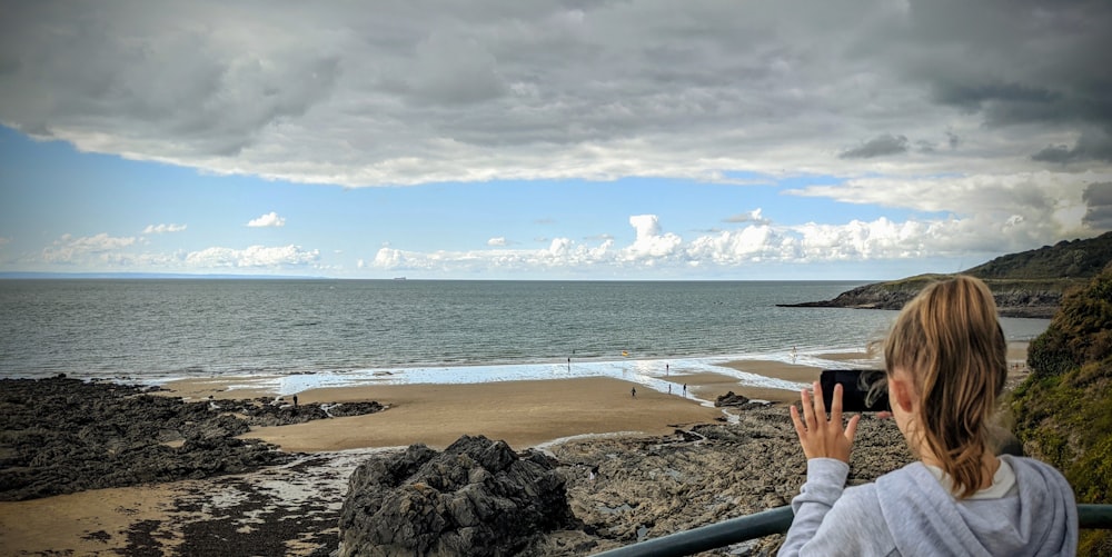 person in gray pants sitting on brown rock near body of water during daytime