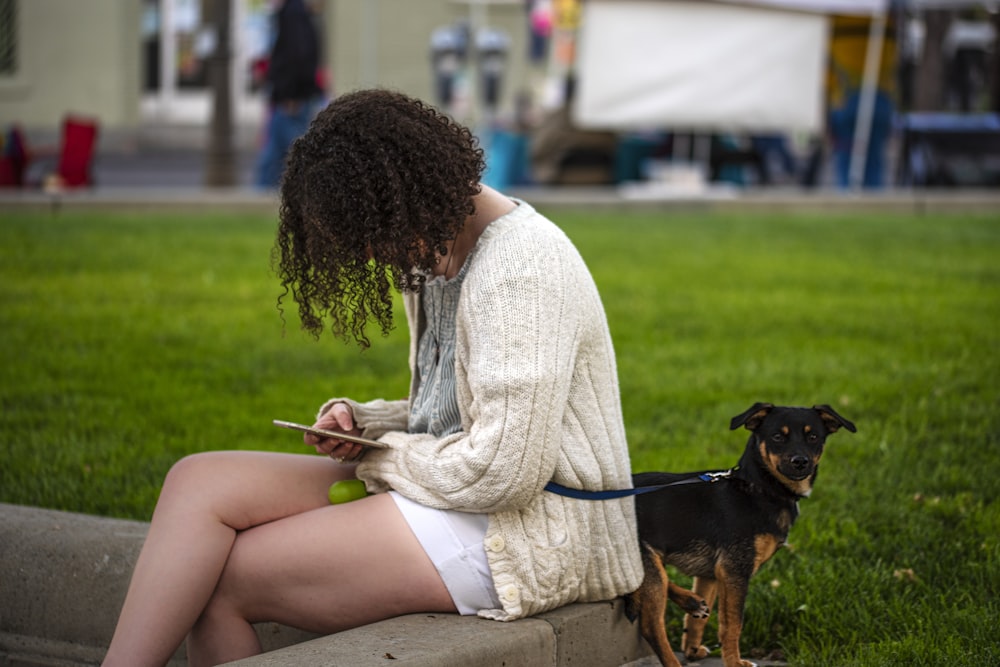 woman in white long sleeve shirt sitting beside black and brown short coated dog on green