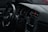 The interior of a modern car is shown, highlighting the steering wheel, dashboard, and part of the driver's door. The dashboard features a digital display with various controls and indicators, and the car appears to be silent and stationary.