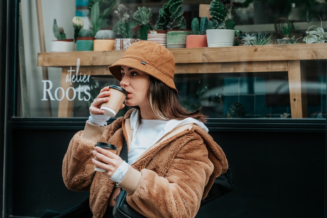 woman in brown coat holding white ceramic mug