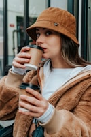 woman in brown coat holding white ceramic mug