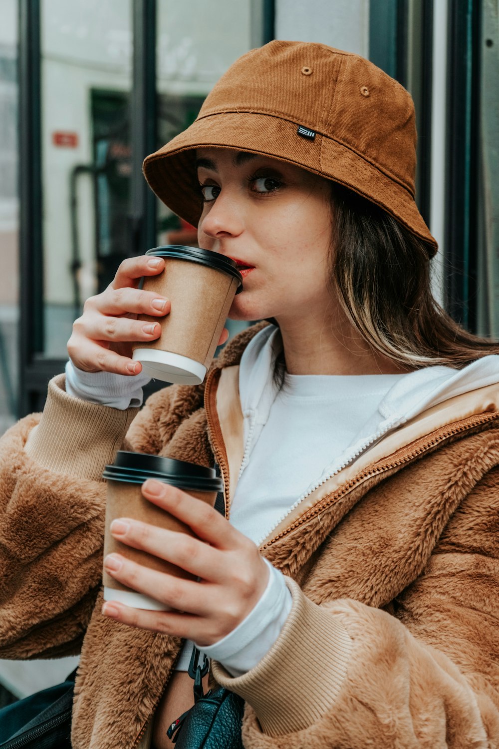 woman in brown coat holding white ceramic mug