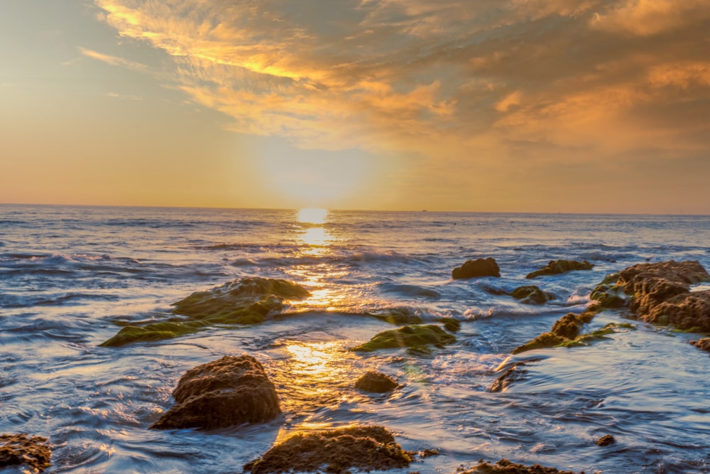 rocky shore under cloudy sky during sunset