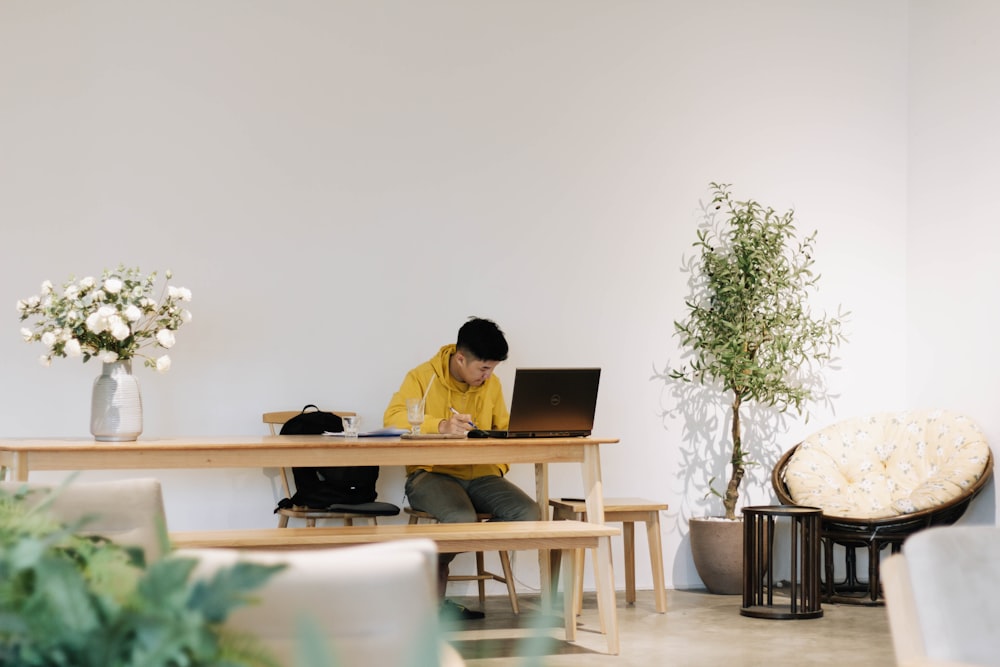 man in yellow dress shirt sitting on chair in front of laptop computer