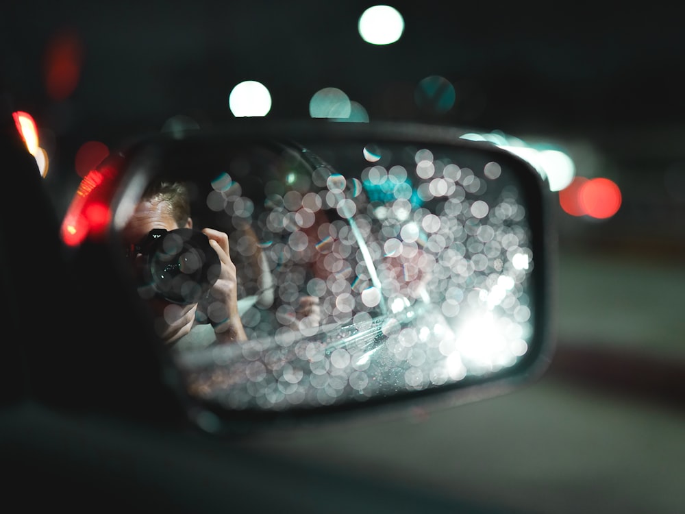 person in black sunglasses taking selfie on car side mirror