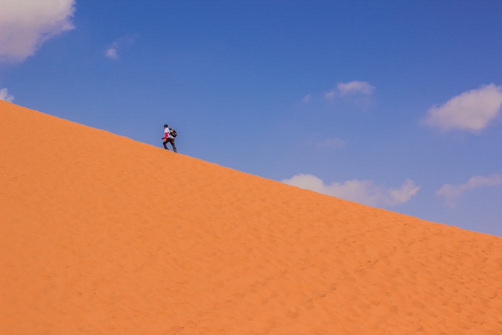 man in black shirt and blue denim jeans walking on brown sand during daytime