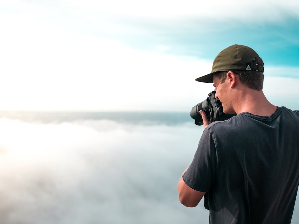 man in black shirt and black cap standing near foggy mountain during daytime