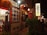 A warmly lit street scene featuring a traditional Asian restaurant with brick walls and decorative lanterns. The entrance displays a menu with images of various dishes and signage in Chinese characters. People are visible near the entrance, adding to the lively atmosphere.