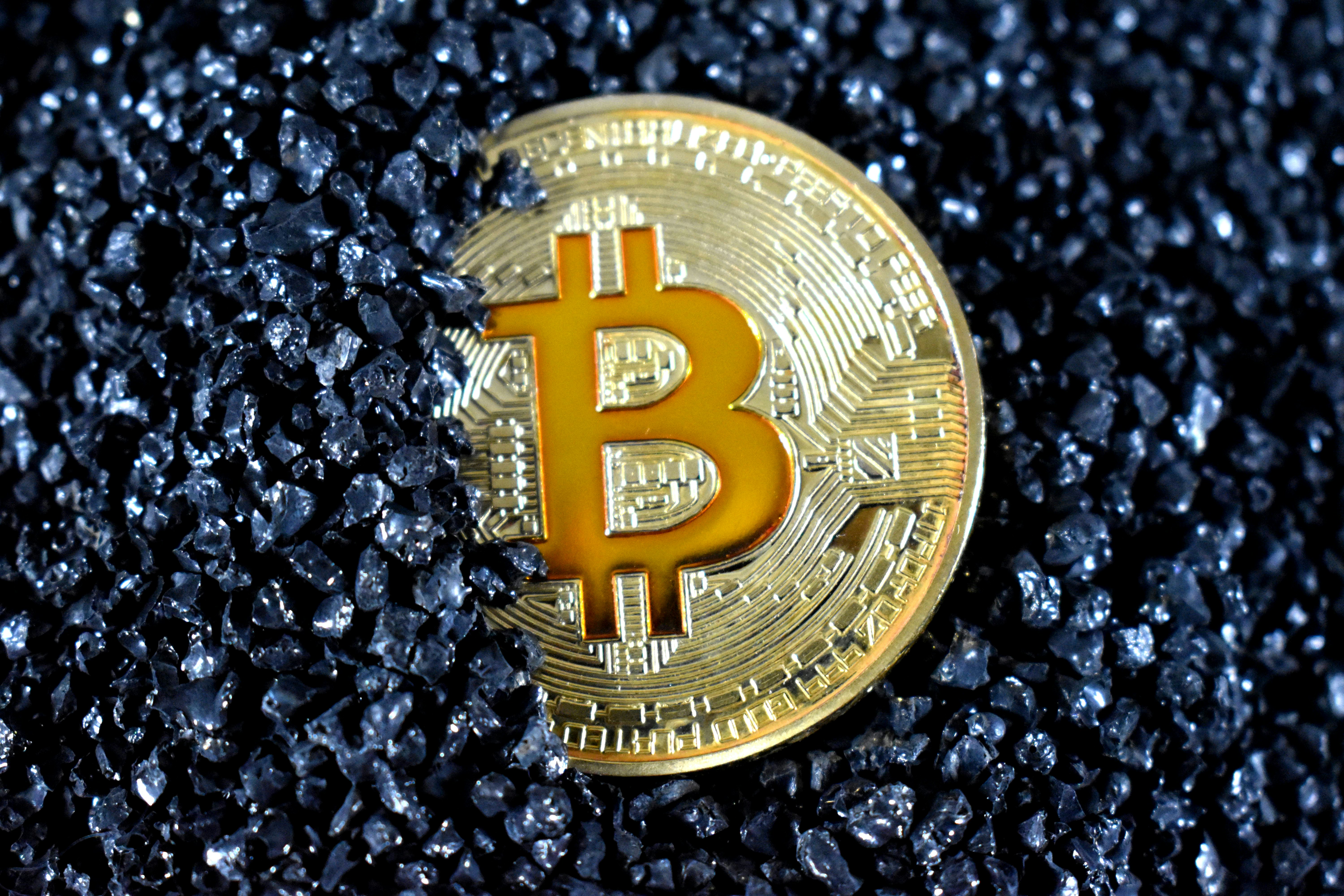 A Bitcoin half-covered in black crystals.