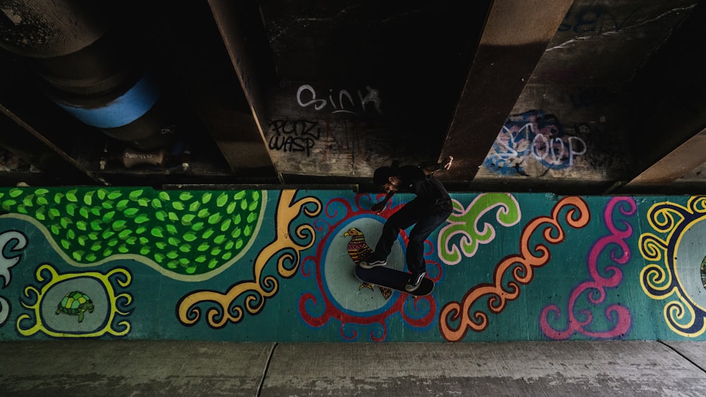 man in black jacket and black pants sitting on green and blue wall