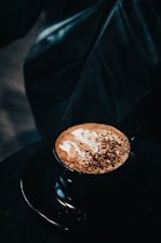 An elegant cup of freshly brewed cappuccino on a matte black saucer, set against a warm beige background.