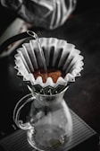 Hands preparing a pour-over coffee with a clean glass carafe capturing the rich brew.