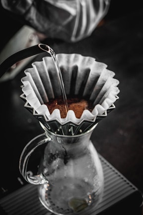 Hands preparing a pour-over coffee with a clean glass carafe capturing the rich brew.