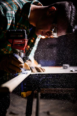 A DIY enthusiast wearing safety glasses, using a power sander on a wooden chair.