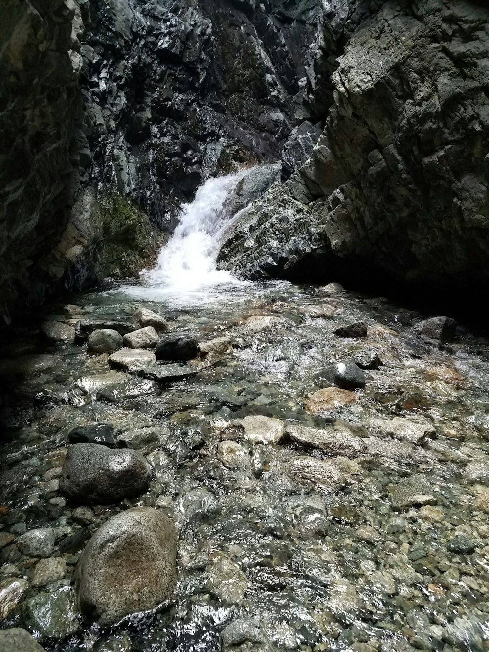 water falls between rocky mountain during daytime