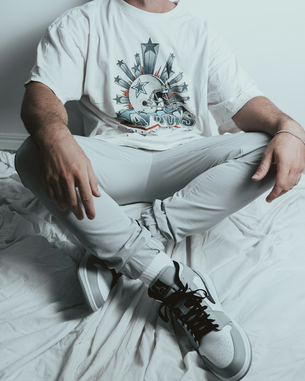 man in white crew neck t-shirt and gray pants sitting on white bed