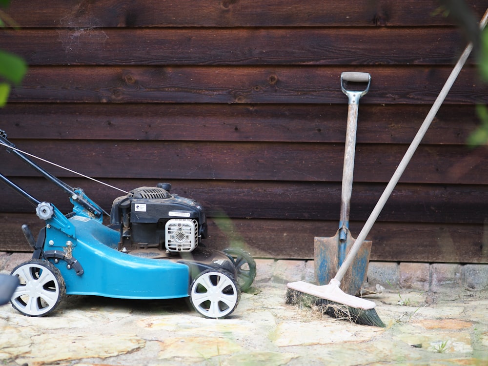 green and black push lawn mower beside brown wooden wall