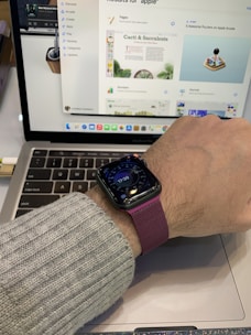A person wearing a smartwatch with a maroon strap, displaying the time as 17:39. The hand is resting on a laptop keyboard, which shows a webpage featuring cacti and succulent content with various app icons visible in the dock.