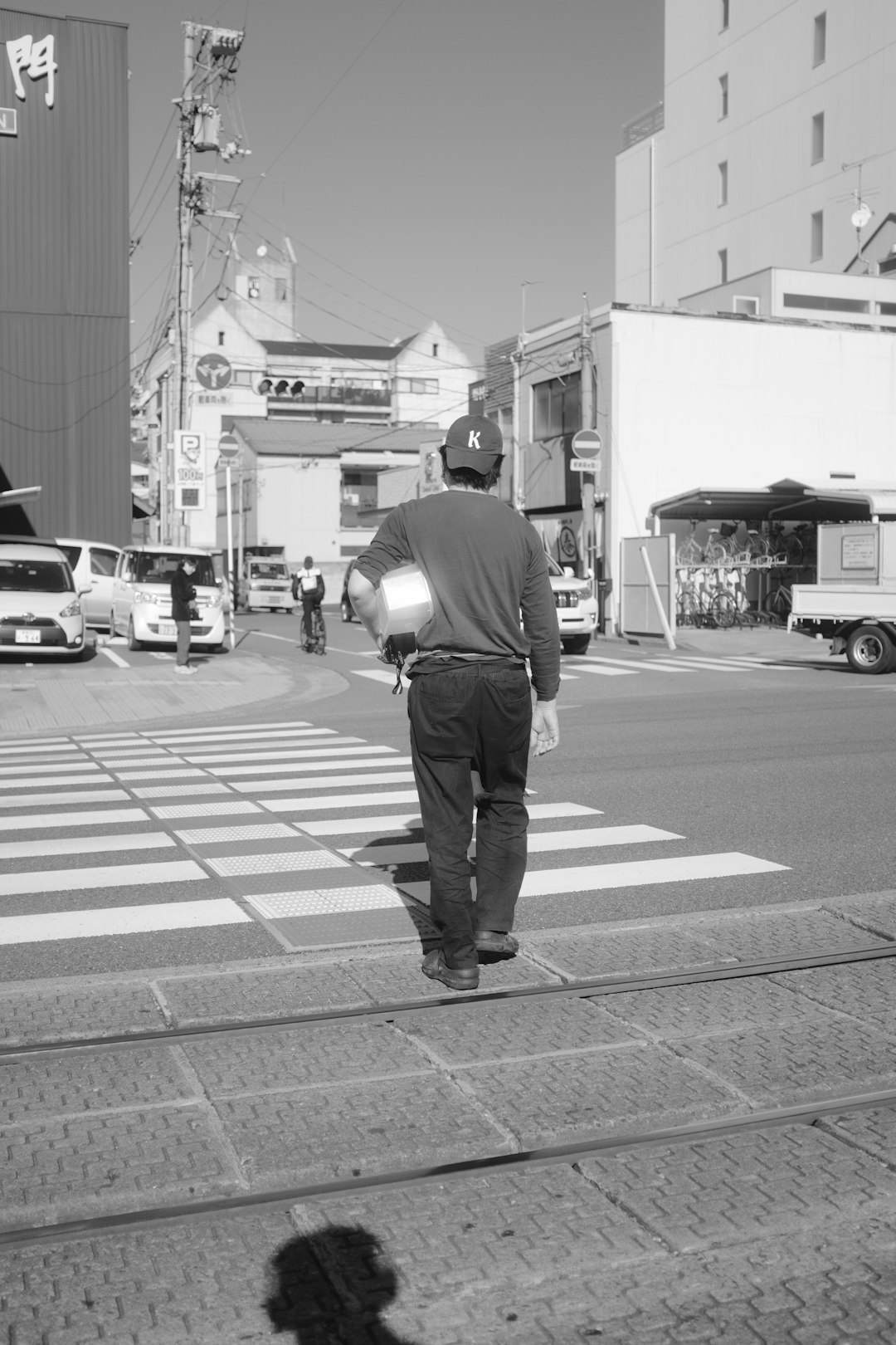 man in black jacket and pants walking on pedestrian lane in grayscale photography