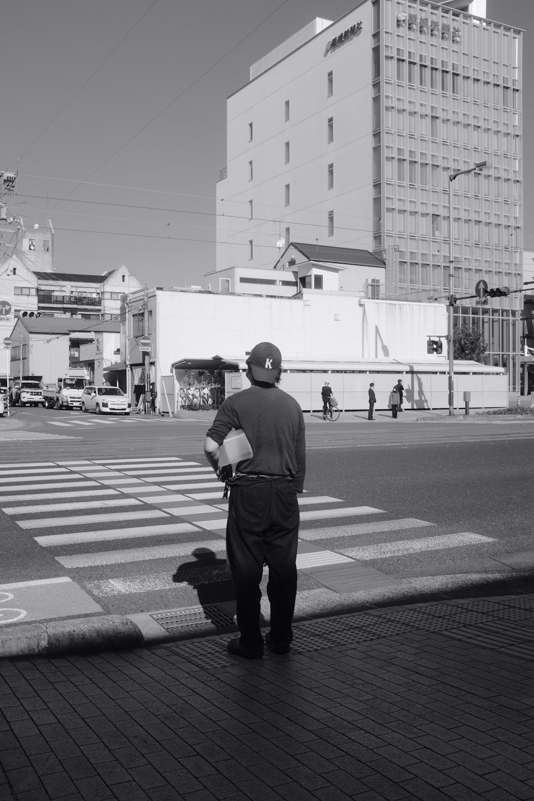 grayscale photo of man in black shirt and pants walking on pedestrian lane