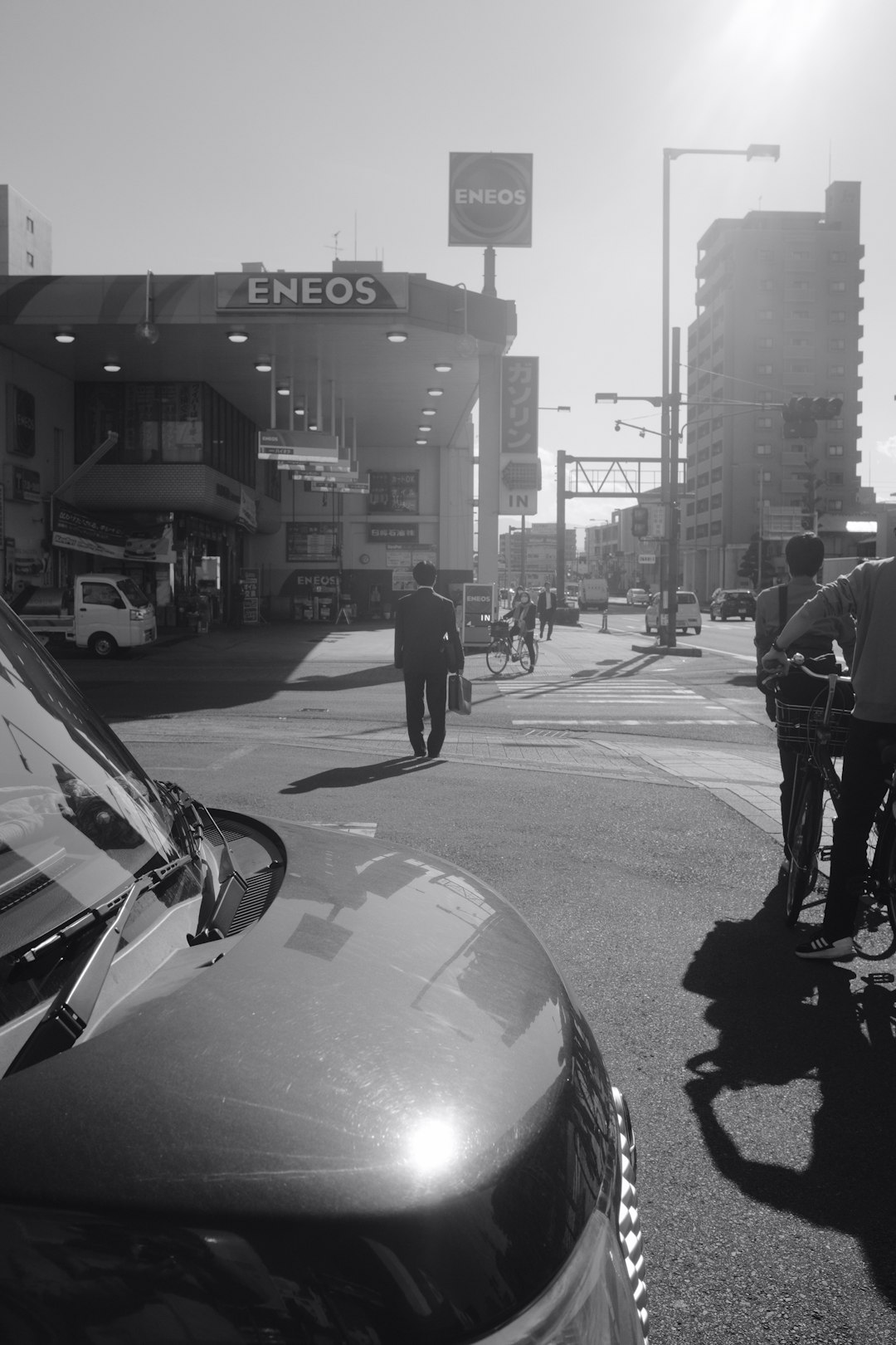 grayscale photo of man walking on sidewalk near car