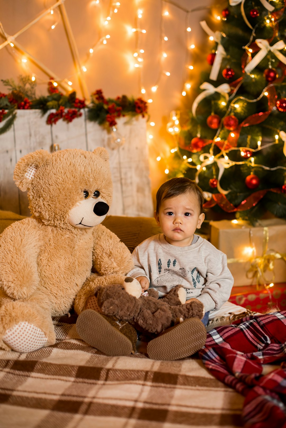 boy in gray sweater sitting beside brown bear plush toy