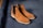 A pair of brown suede Chelsea boots rests on a dark blue surface. The boots feature a classic design with elastic side panels and a light-colored sole.