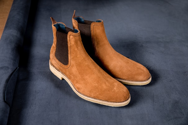 A sleek pair of black Chelsea boots resting on a polished dark wood surface, highlighting the fine grain of the leather