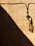 A textured beige wall with a prominent diagonal shadow. An old, weathered glass insulator is attached to the wall, casting its own shadow. Black wires run horizontally and vertically, creating a pattern against the wall.