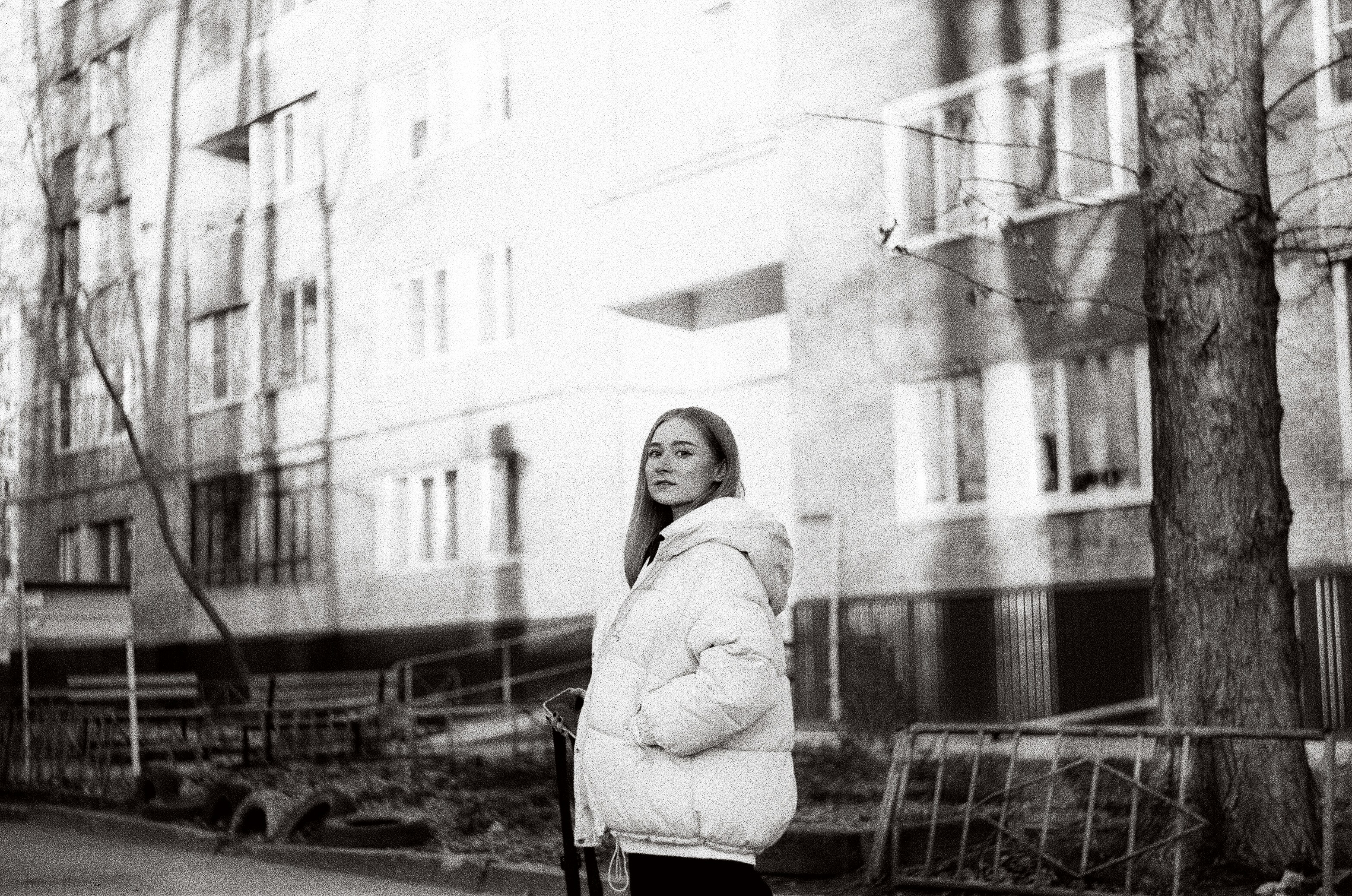 Frau im Mantel in der Nähe des Gebäudes in Graustufenfotografie