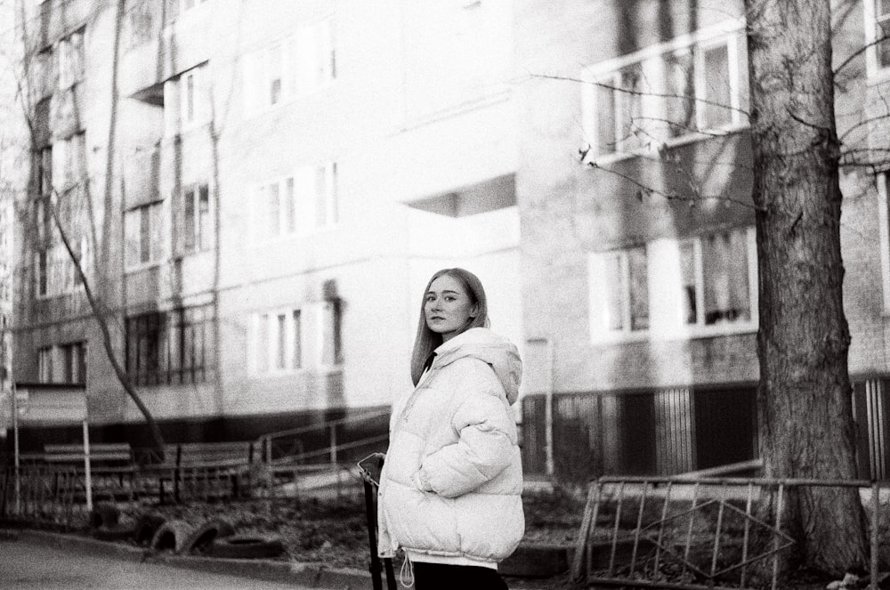 donna in cappotto in piedi vicino all'edificio in fotografia in scala di grigi