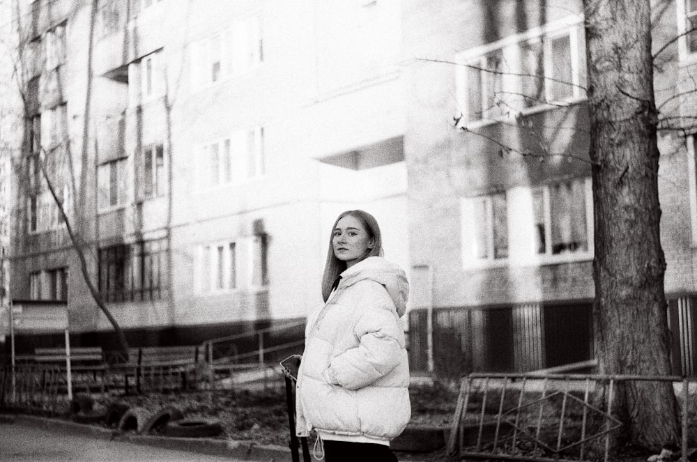 woman in coat standing near building in grayscale photography