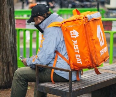 man in gray and orange jacket and black pants sitting on brown wooden bench