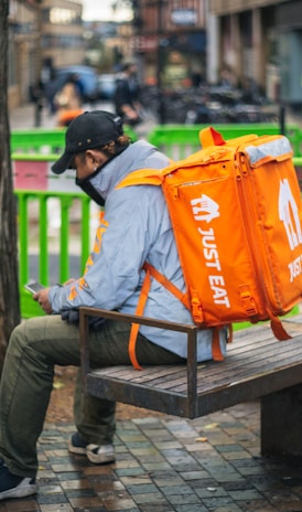 man in gray and orange jacket and black pants sitting on brown wooden bench