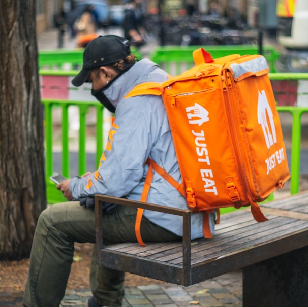 man in gray and orange jacket and black pants sitting on brown wooden bench