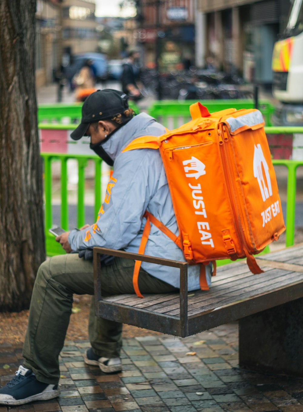 man in gray and orange jacket and black pants sitting on brown wooden bench