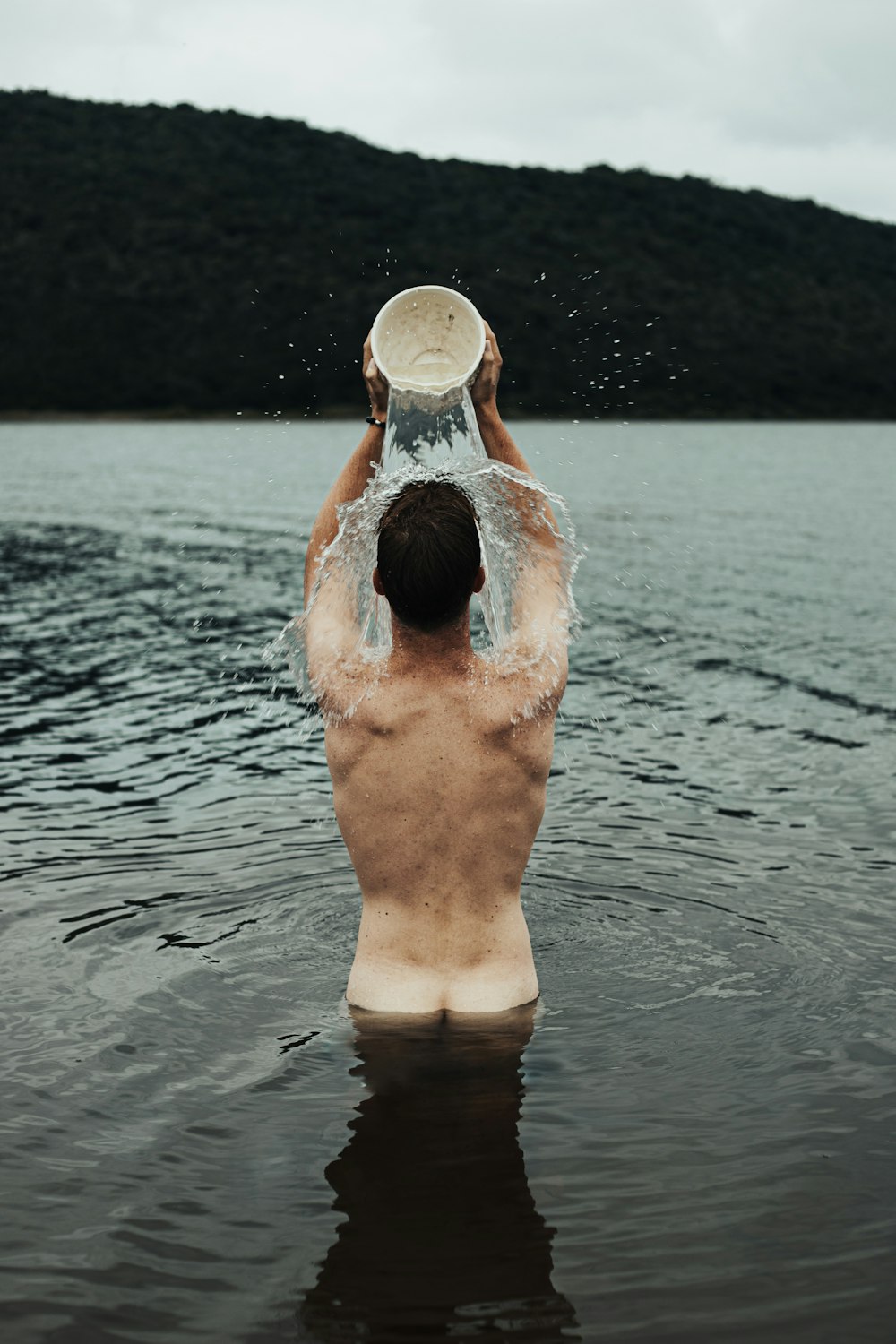 man in water holding white plastic bucket