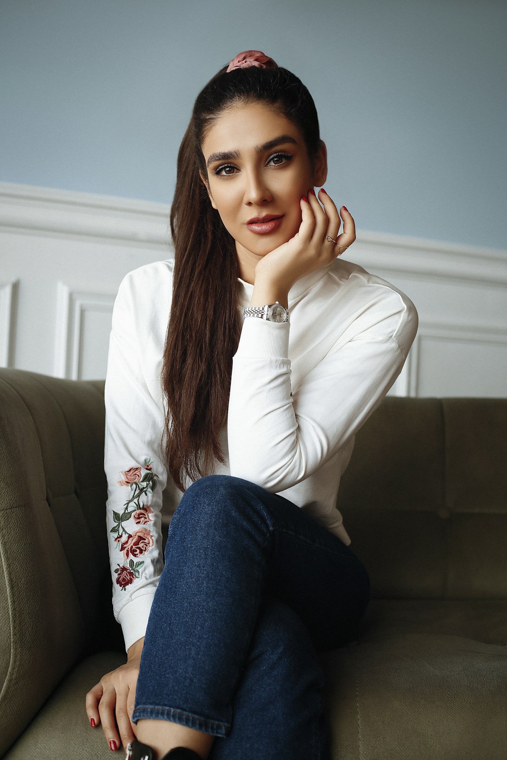 femme en chemise à manches longues blanche et jean en jean bleu assise sur un canapé gris