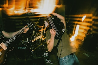 A dynamic and intense moment of a live rock performance features musicians playing guitars energetically. The scene includes motion blur and light streaks, suggesting movement and excitement. The drummer is visible in the background, and concert lighting creates a dramatic atmosphere.