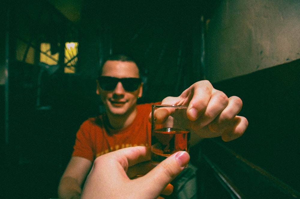 Hombre con camiseta marrón de cuello redondo sosteniendo un vaso transparente para beber