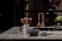 A modern kitchen countertop made of stone with a white ceramic holder containing wooden cooking utensils. In the foreground, there is a blue bowl and a small green cup. Three wooden kitchen utensils are hanging on a black metal bar.
