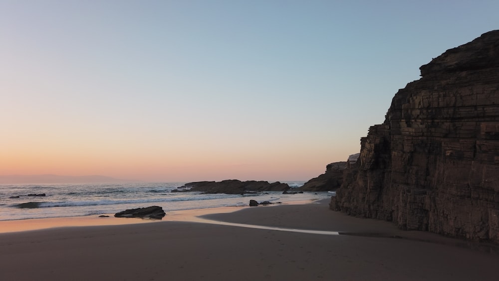 Formação rochosa marrom na praia durante o dia