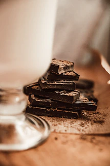 Close-up of glossy dark chocolate squares stacked neatly on a rustic wooden board.