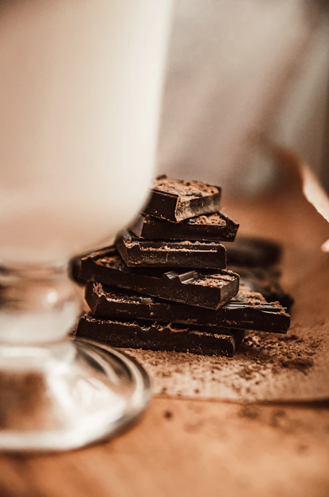 Close-up of glossy dark chocolate squares stacked neatly on a rustic wooden board.